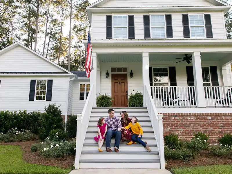 Happy family sitting together on the steps of a front porch in their white, mid-class home